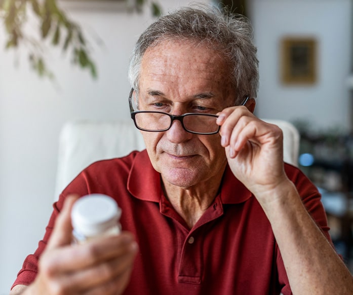 Older man reading prescription bottle label.